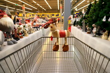 Funny Christmas Deer On Supermarket Trolley. Shopping In The Shop Before The New Year, Sale. A Basket In Wholesale Store, Background Of Blurred Shelves With Groceries And Goods.