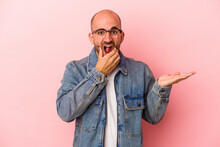 Young Caucasian Bald Man Isolated On Pink Background  Holds Copy Space On A Palm, Keep Hand Over Cheek. Amazed And Delighted.