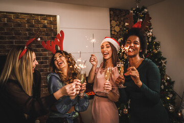 Wall Mural - Multi ethnic Female Friends Playing With Sparklers And Making Toast As During Christmas Home Party