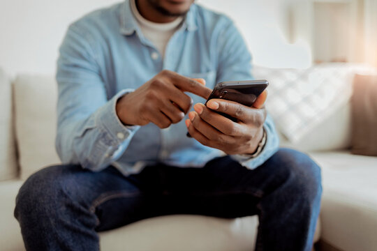 Cropped shot of an black man using a smartphone while sitting indoors. Cropped shot of an handsome businessman sitting alone in his home office and texting on his cellphone. Copy space.