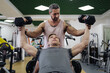 A personal trainer motivates the client to lift heavy dumbbells in the gym. Personal workout hour with personal coach