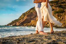 Close Up Legs Photo. Couple In Love Standing On The Sandy Beach With The Sea At The Blurred Background. 