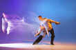 © master1305 - Young graceful dancers, flexible man and woman dancing ballroom dance isolated on gradient blue purple background in neon mixed light