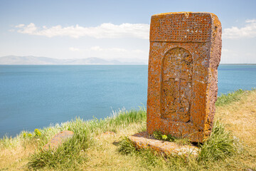 Wall Mural - Ancient traditional carved khachkar or cross-stone installed near Hayravank Monastery with armenian Sevan lake in the background