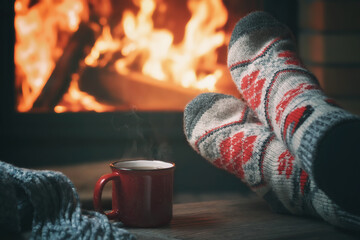 Wall Mural - Girl resting and warming her feet by a burning fireplace in a country house on a winter evening