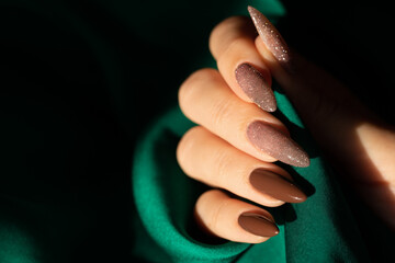 Female hand with a beautiful long nails in brown and shimmer color on a green silk background