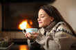 © Antonioguillem - Woman in winter drinking coffee beside a fireplace