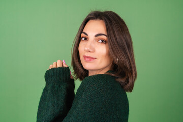 Wall Mural - Young woman on a green background in a cozy big knitted sweater cute smiling