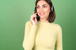 © Анастасия Каргаполов - Young woman on a green background in a yellow sweater manager, support service worker, salesperson, with pleasure accepts calls from customers