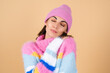 © Анастасия Каргаполов - Young woman on a beige background in a bright multi-colored cozy knitted sweater and a hat comfortably hugs herself, warmth and comfort
