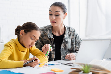 Poster - Mother in military uniform pointing at notebook near daughter and notebooks at home