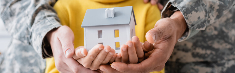 Poster - Cropped view of parents in military uniform holding model of house with daughter, banner