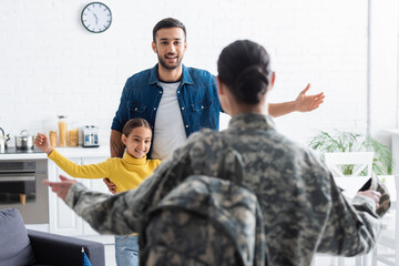 Smiling family looking at blurred mother in military uniform at home