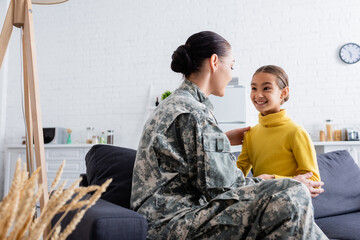 Canvas Print - Woman in camouflage uniform looking at daughter on couch at home