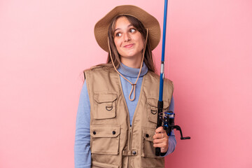 Wall Mural - Young caucasian fisherwoman holding a rod isolated on pink background dreaming of achieving goals and purposes