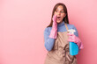 Young caucasian cleaner woman holding spray isolated on pink background is saying a secret hot braking news and looking aside