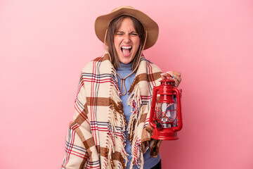 Wall Mural - Young caucasian woman holding vintage lantern isolated on pink background screaming very angry and aggressive.