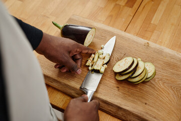 Wall Mural - Top view close up of unrecognizable African-American man cutting aubergine while cooking dinner on wooden table, copy space