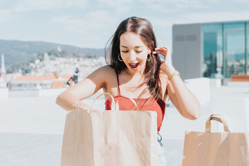 Happy beautiful african modern woman looking inside shopping bag surprised about what is inside. On city street mall. Copy space, Christmas new year shopping presents concept, new clothes shopping 