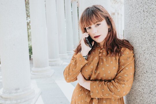 Serious pensive hipster redhead young woman with smart phone. Copy space for text image. Casual dressing in autumnal tones. red lips and modern hairstyle, bright day.