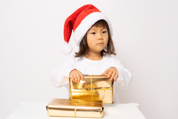 Wall Mural - Little asian girl in santa hat sitting with gift boxes isolated over white background.