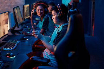 Side view of Asian cybersport gamer in headphones playing mobile game on cellphone in contemporary e-sports club