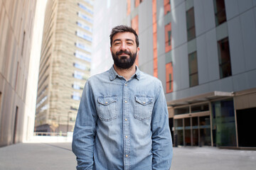 Attractive business man looking at camera outdoors near large office building. Young casual dressed young man with cheerful smile, entrepreneur, executive, male person Success concept.