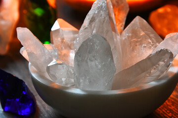 Wall Mural - An image of a white bowl filled with a variety of clear quartz crystals with a glowing pink salt lamp in the background. 