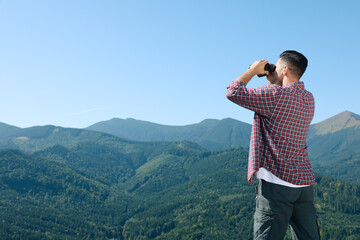 Wall Mural - Man looking through binoculars in mountains on sunny day