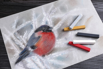 Poster - Colorful chalk pastels and beautiful painting of bullfinch on black wooden table, top view