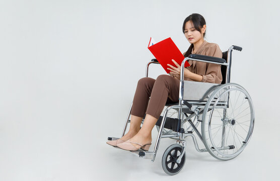 Pretty young Asian girl as disability patient on hospital wheelchair study clinical report by reading physical health care and medical rehabilitation instruction for transporting injured person