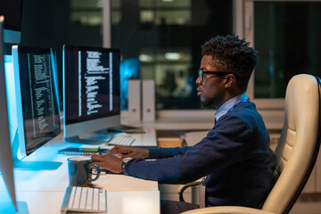 Poster - Young it-engineer of African ethnicity working with coded data while sitting in armchair in front of computer in office