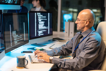 Poster - Serious elegant businessman typing and looking at coded data on computer screen while decoding it in office environment