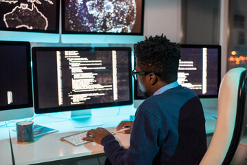 Poster - Young African male software developer working late in front of computer screen with coded data in office environment