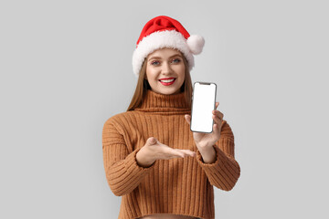 Wall Mural - Beautiful young woman in Santa hat and with mobile phone on grey background