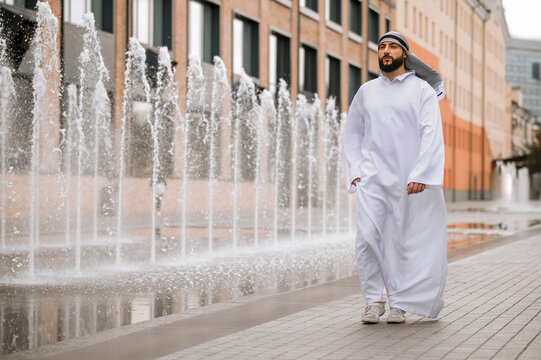 Middle eastern young man in traditional clothing walking along the street