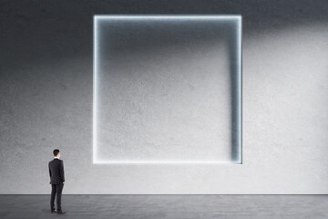Poster - Businessman standing in minimalistic concrete interior with abstract clean square poster on wall. Mock up. Exhibition, gallery and art concept.