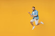 © ViDi Studio - Full body young smiling happy caucasian man 20s wear blue shirt jump high point index finger on workspace area copy space isolated on plain yellow background studio portrait. People lifestyle concept.