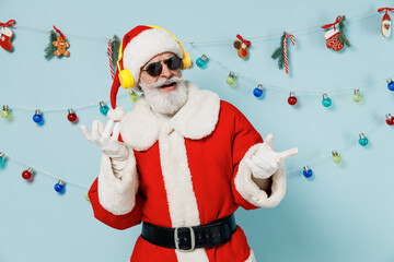 Wall Mural - Old Santa Claus man 50s wear Christmas hat red suit clothes headphones listen to music dancing isolated on plain blue background studio. Happy New Year 2022 celebration merry ho x-mas holiday concept.