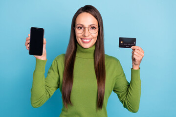 Poster - Photo of shiny cute woman wear green turtleneck glasses holding bank card modern device empty space isolated blue color background