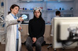 Neurologist doctor showing monitor with brain activity to woman patient with eeg scanner on head during neuroscience experiment in medical lab. Scientist physician analyzing nervous system evolution