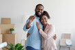 © Prostock-studio - Happy smiling young african american loving family hugging in new home among boxes and showing house keys