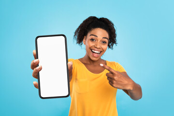 Smiling black lady demonstrating smartphone with mockup, pointing at empty screen on blue background, space for app