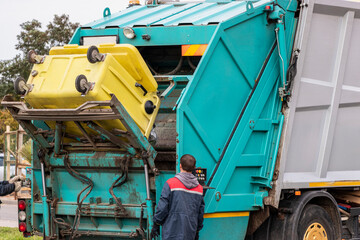 Fototapete - A garbage truck picks up garbage in a residential area. Workers load a container with garbage. Separate collection and disposal of garbage.
