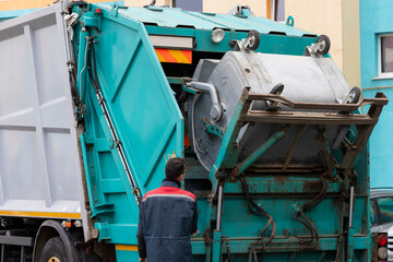 Fototapete - A garbage truck picks up garbage in a residential area. Workers load a container with garbage. Separate collection and disposal of garbage.