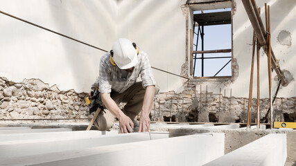 Wall Mural - man at work, construction worker wear a helmet, check the measurements and distances of the beams at the base of the foundations of the second floor of house, in renovation building site background