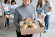 Elderly woman holding box with donations food, cans and packages with grains and pasta, closeup, crop