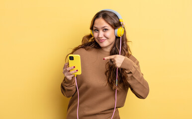 Wall Mural - hispanic pretty woman looking excited and surprised pointing to the side. headphones and smartphone concept