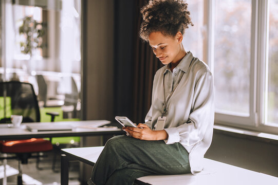 Curly-haired woman sitting on the table with a phone in hands