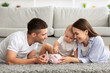 © Prostock-studio - Family Finances. Parents And Infant Child Putting Coins To Piggybank At Home